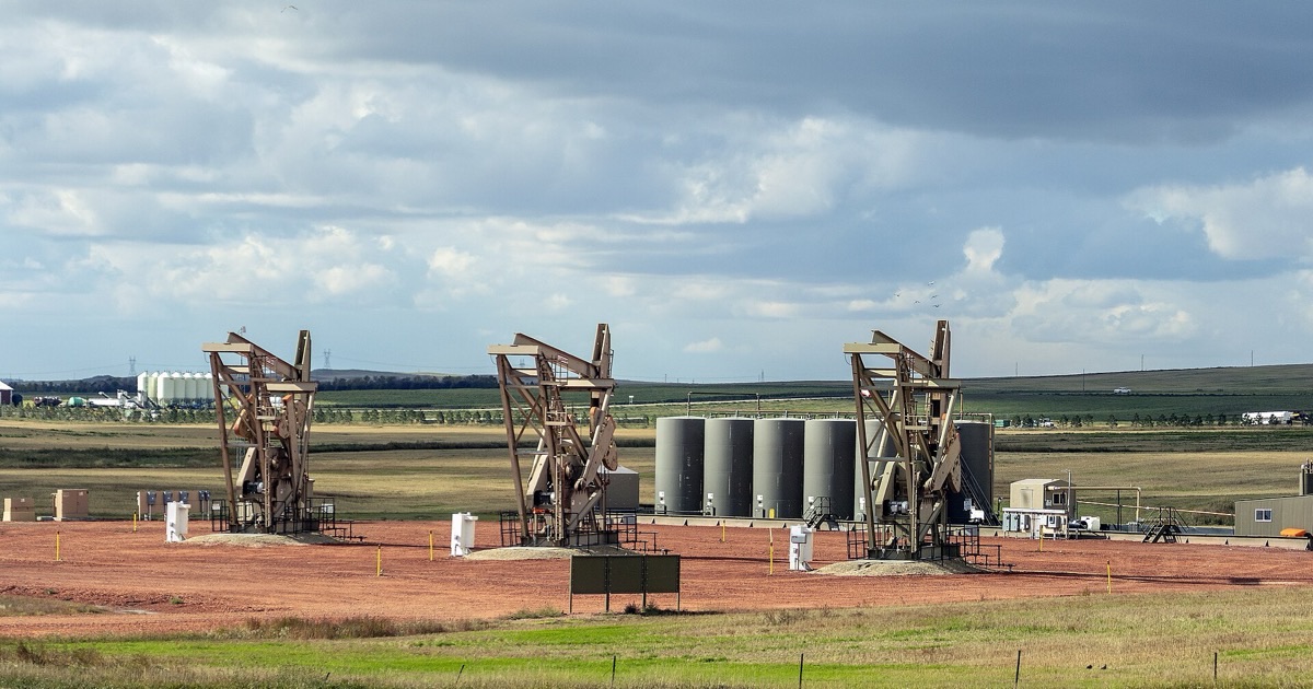 Three oil pumpjacks operating in a North Dakota field under a cloudy sky.
