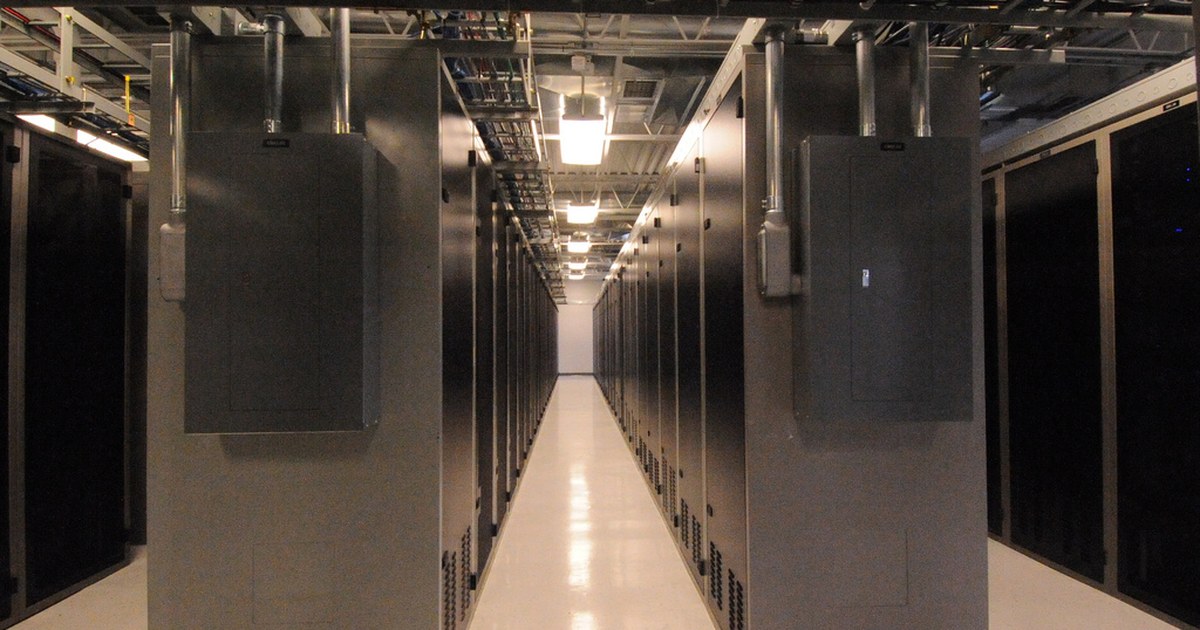 A brightly lit aisle between server cabinets inside a working data center.