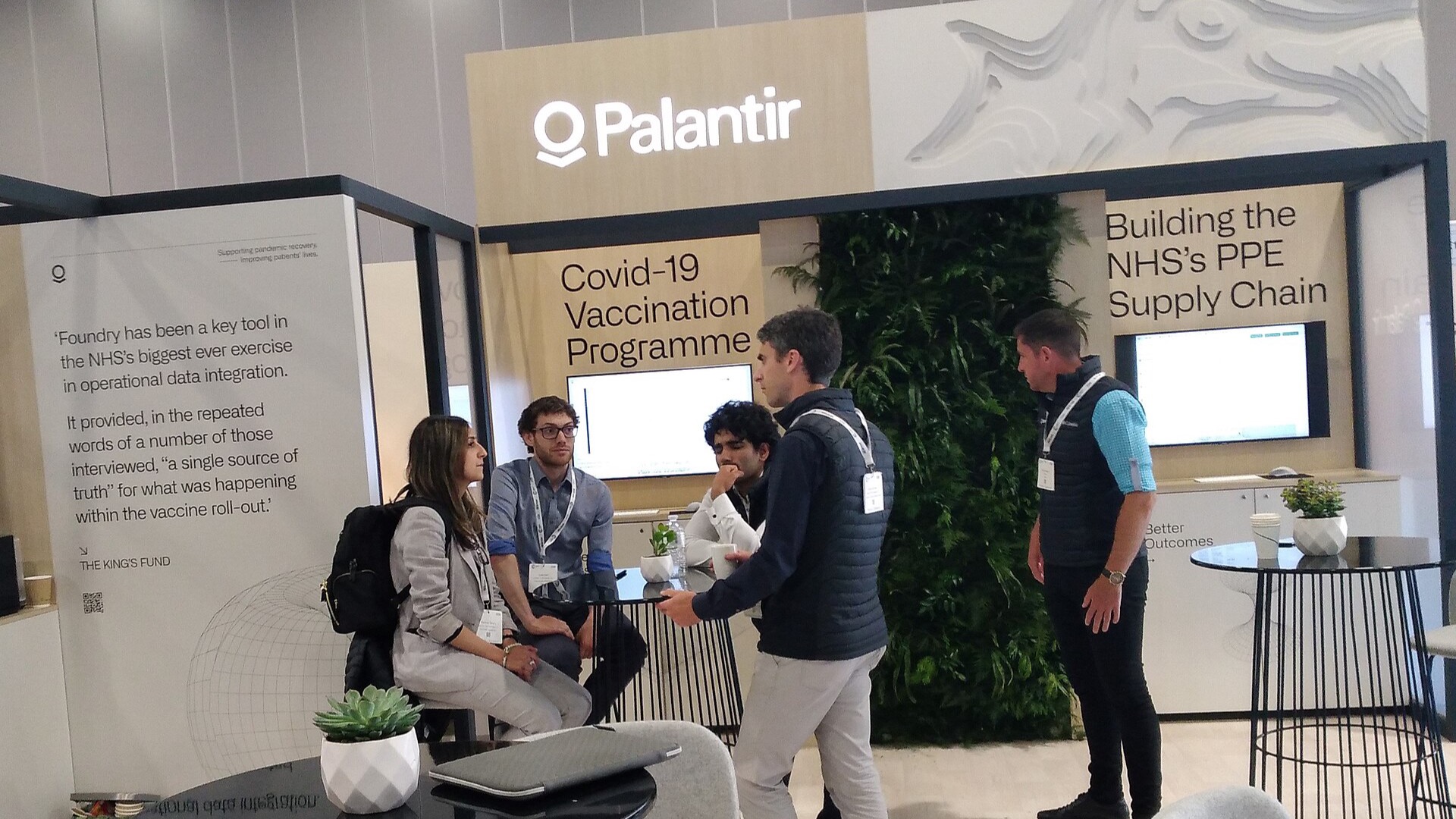 Attendees at Palantir's stand during the 2022 NHS Confederation conference, with operational-data displays behind them.