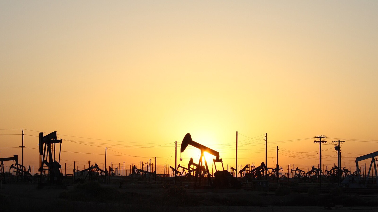 Oil pumpjacks silhouetted across an active field at sunset