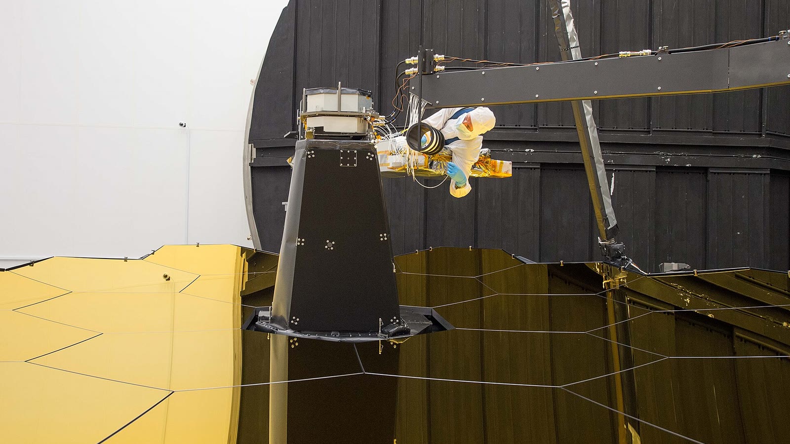 An aerospace engineer connects fiber-optic cables above the James Webb Space Telescope mirror