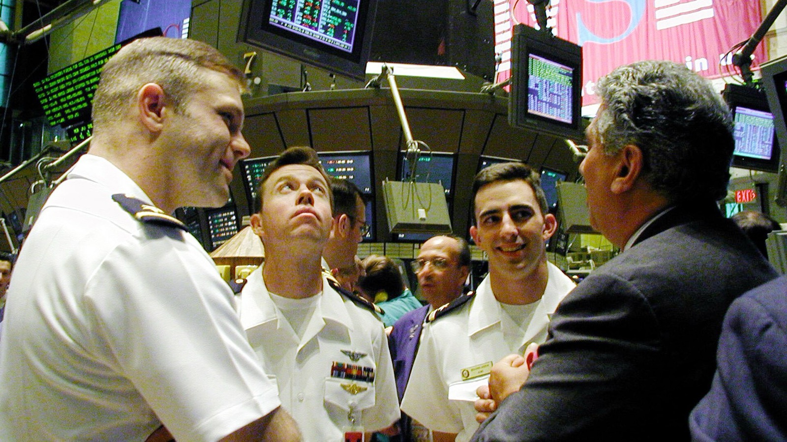 U.S. Navy ensigns speak with a trader on the New York Stock Exchange floor