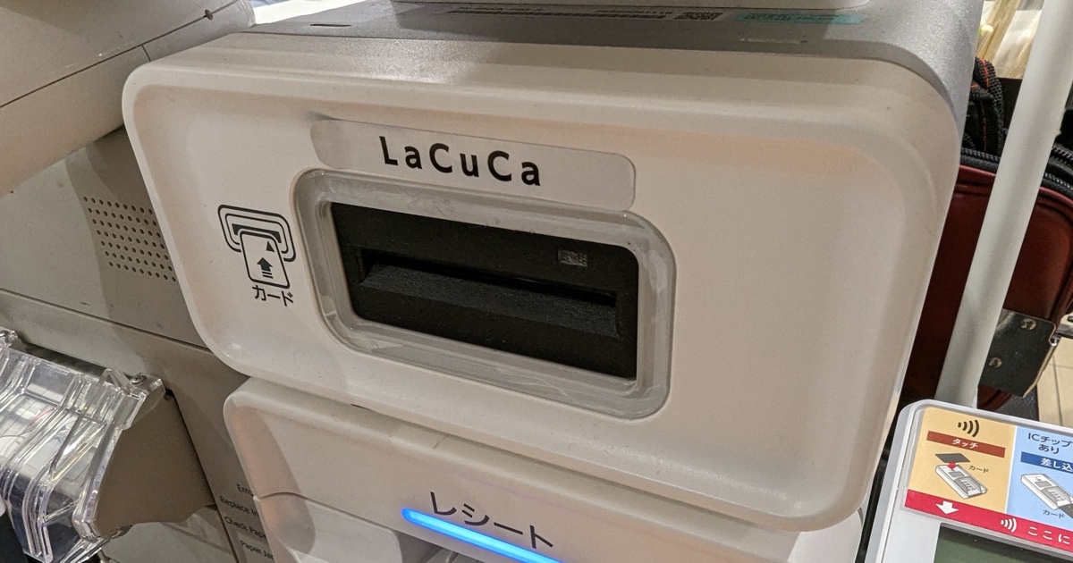 A white in-store payment terminal with a card slot and contactless-card marking beside a supermarket checkout.