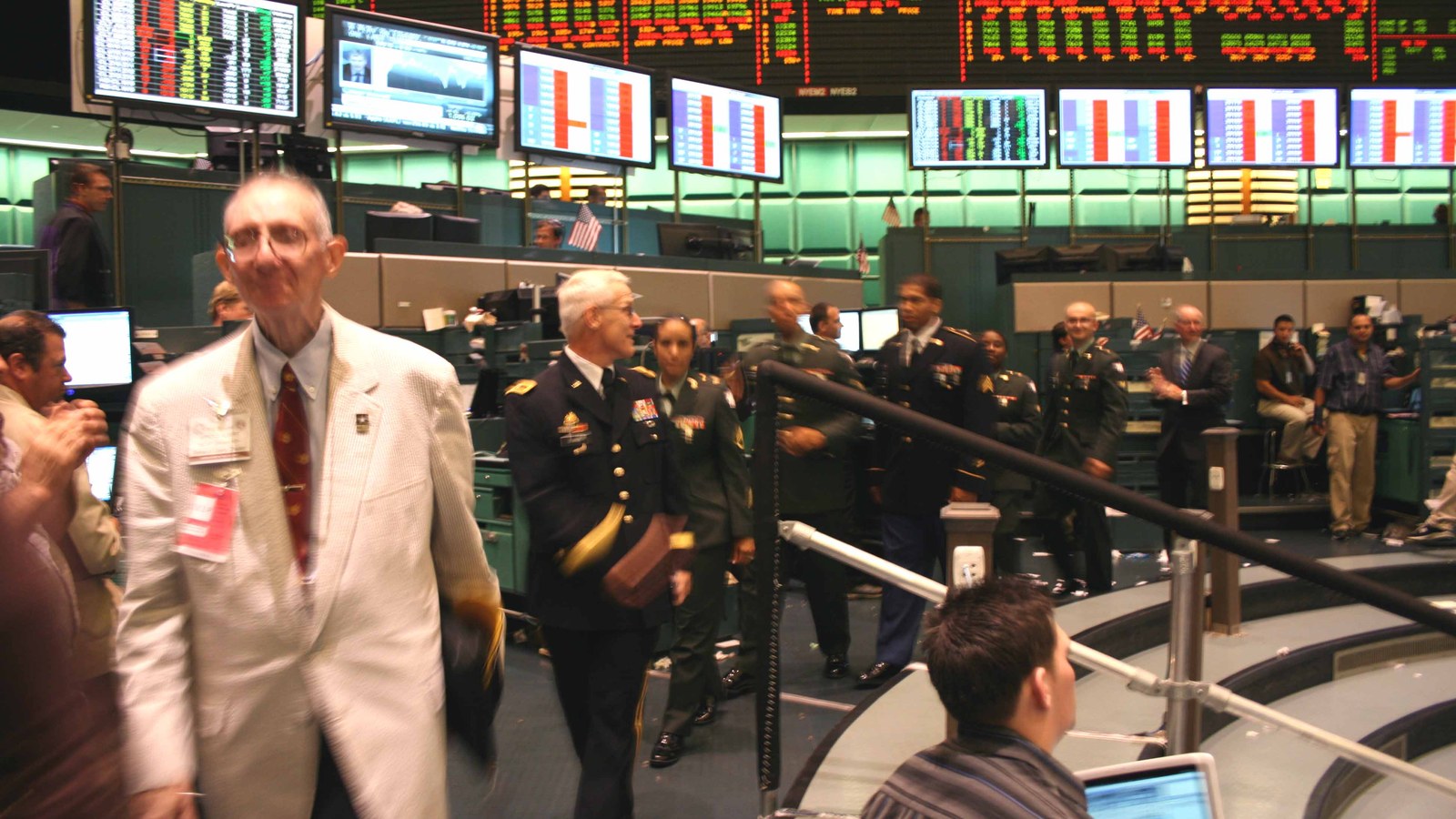Uniformed visitors and staff cross a busy New York trading floor beneath market screens