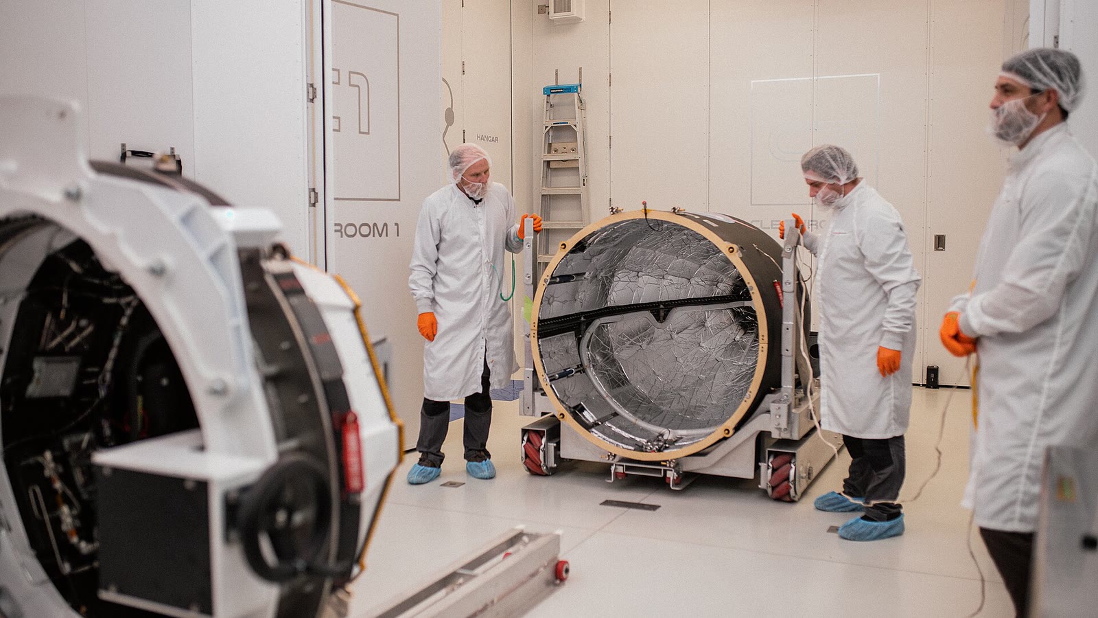 Des techniciens en salle blanche entourent du matériel spatial cylindrique dans une installation de Rocket Lab