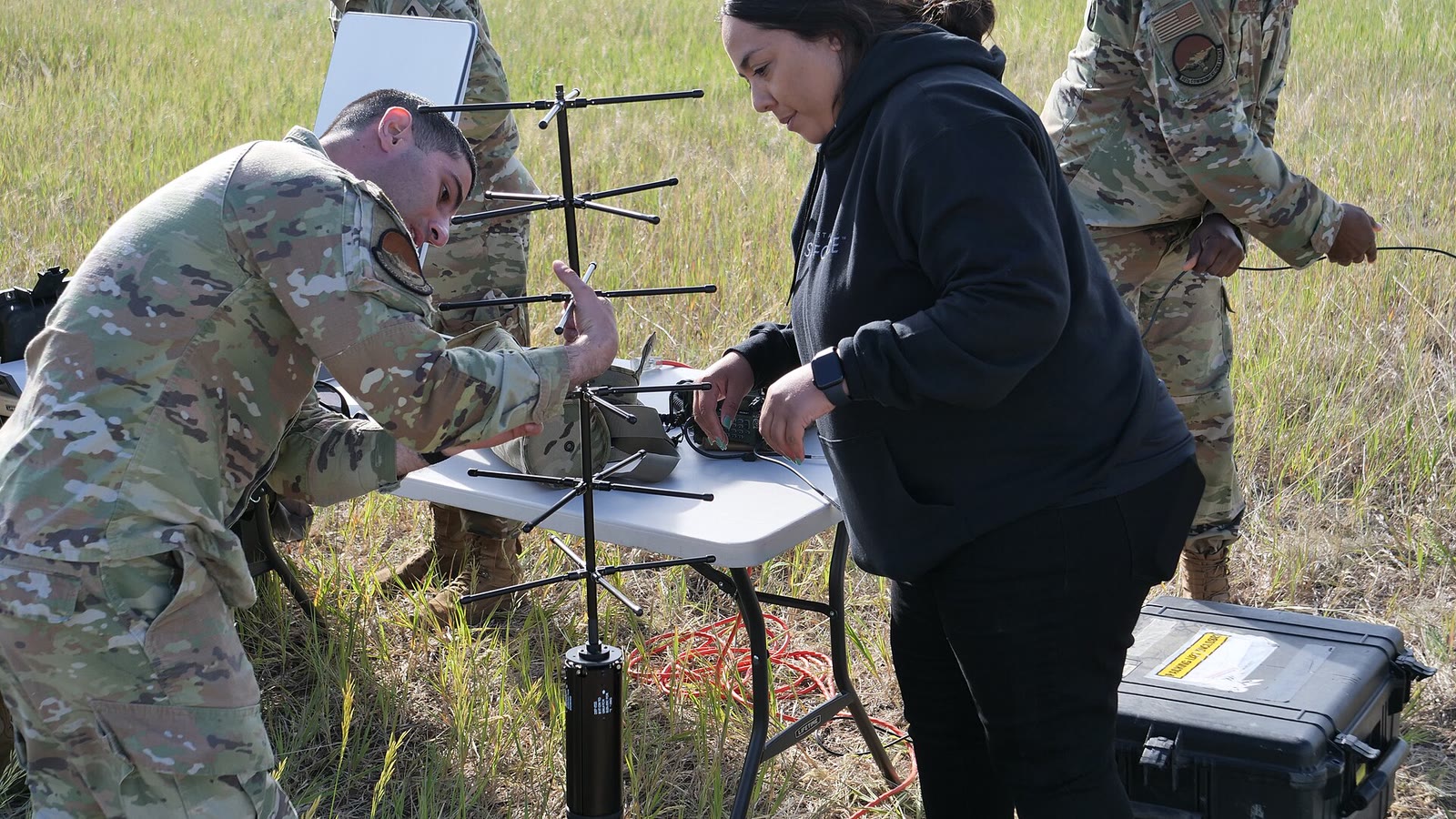 Des membres de la Space Force et une spécialiste civile assemblent une antenne de station satellite mobile sur le terrain