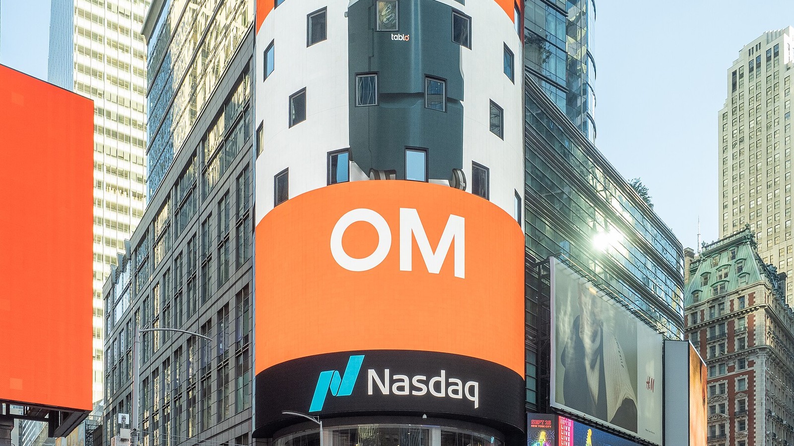 Large orange Nasdaq MarketSite display on a glass tower at a busy New York intersection