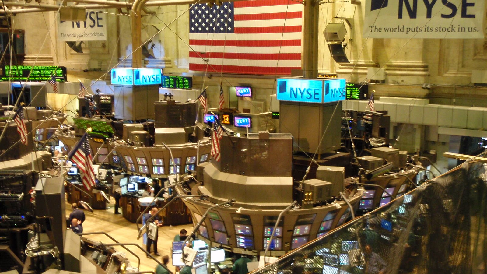 A wide view of the New York Stock Exchange floor with trading posts, screens, American flags and NYSE signs
