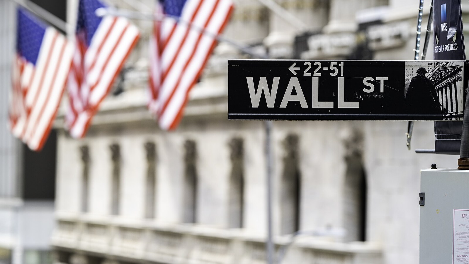 A black Wall Street sign in sharp focus with American flags blurred behind it