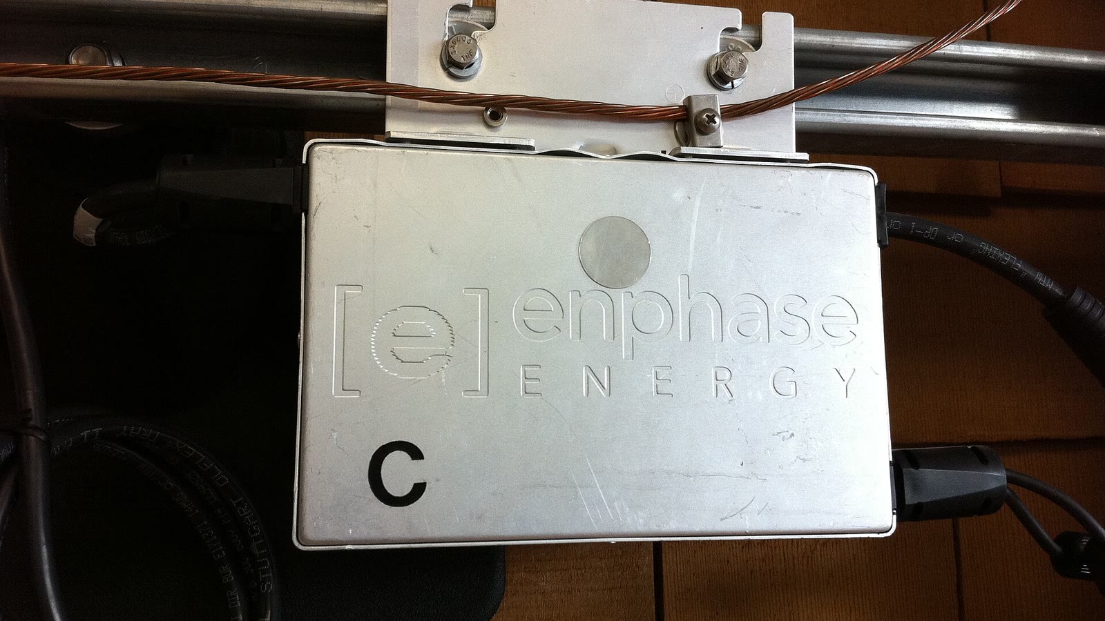 An Enphase M190 solar microinverter mounted beneath a panel rail during installation