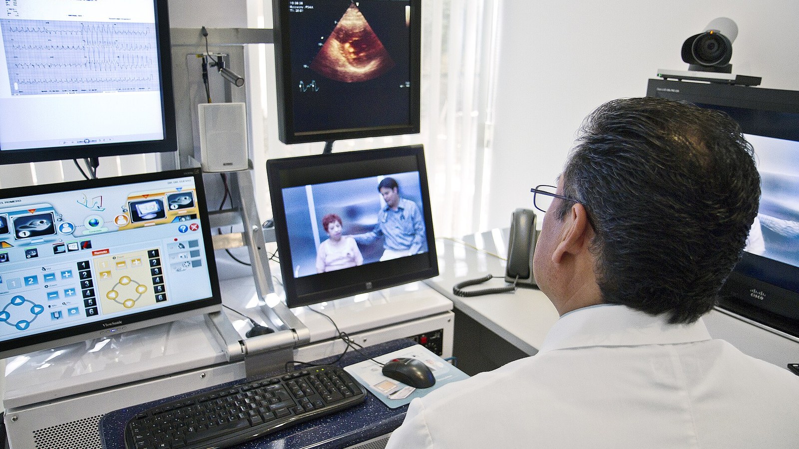 A physician conducts a remote consultation beside medical imaging and video-conferencing equipment
