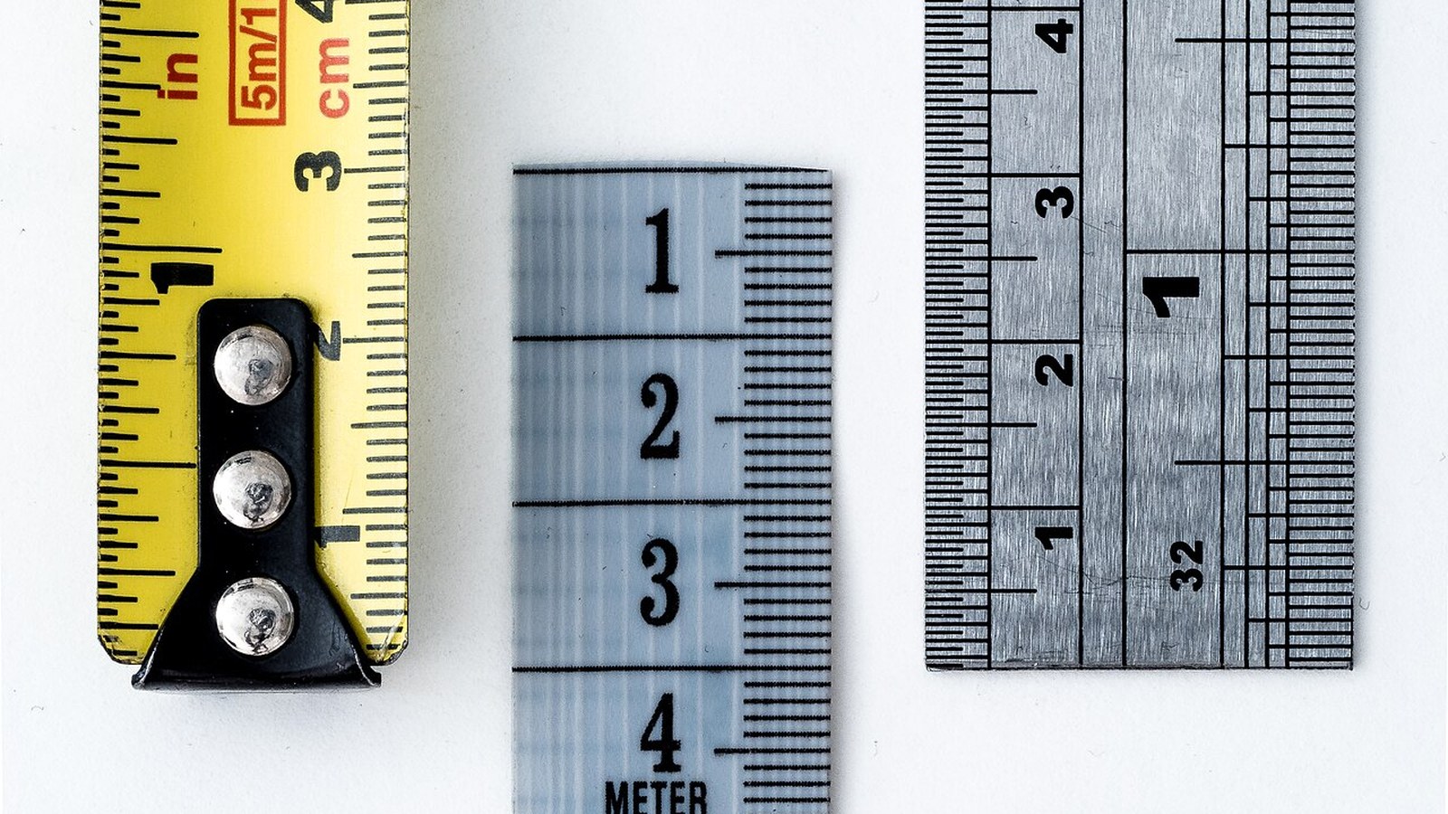Close-up of three measuring tapes and rulers aligned on a white surface