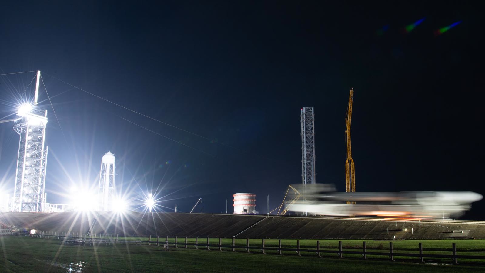A long-exposure night photograph of a SpaceX Falcon 9 and Dragon moving past NASA's Launch Complex 39A.