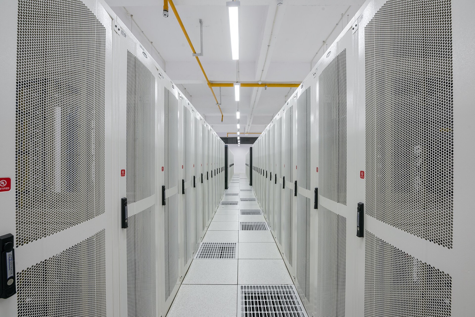 A long, brightly lit aisle between rows of white server racks in a data center