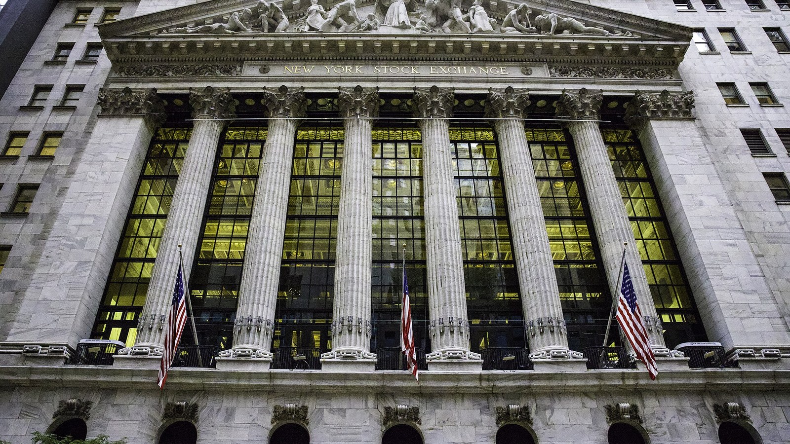 The New York Stock Exchange facade with stone columns, illuminated windows and American flags.