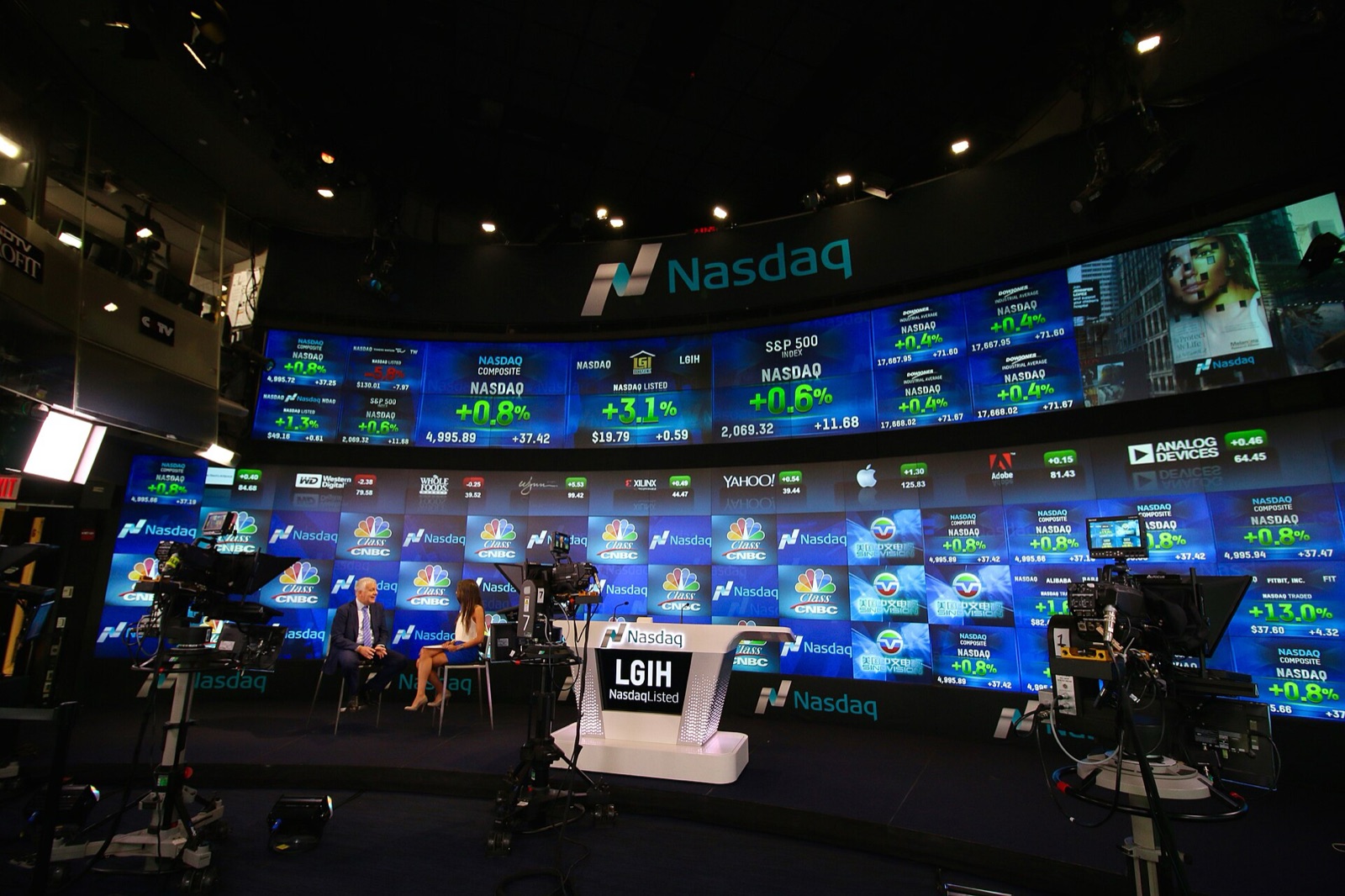 Nasdaq MarketSite studio in New York, with a wall of screens showing stock quotes behind a TV interview set
