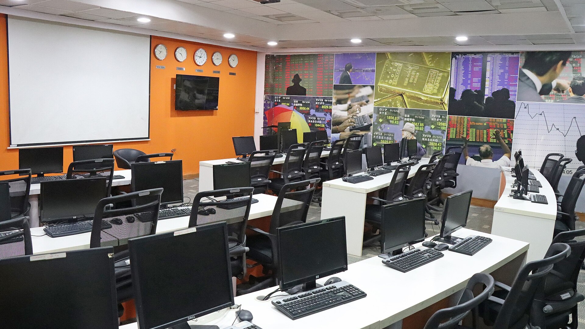 An empty global asset trading room with rows of computer workstations and a wall of market-data screens