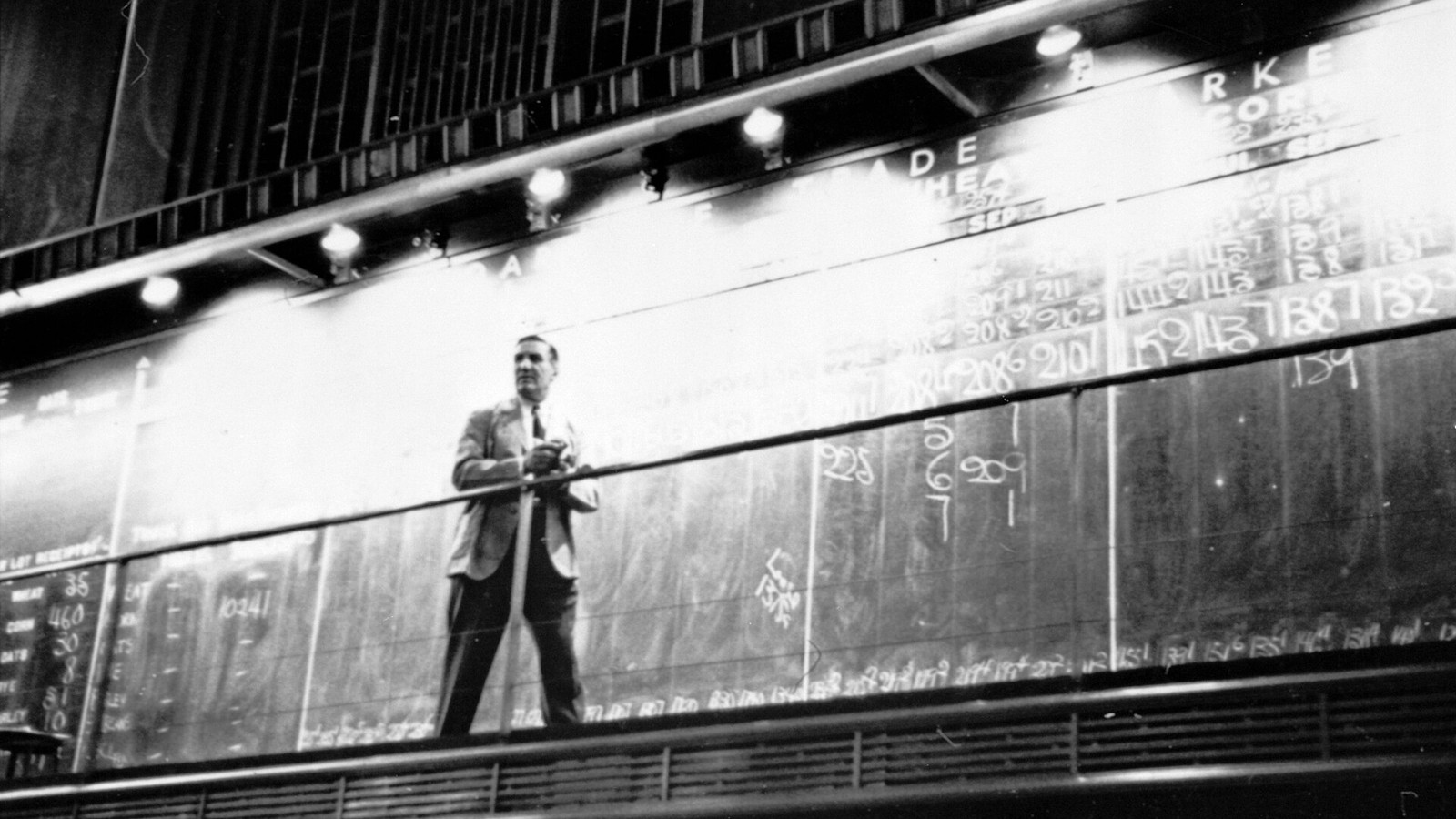 Black-and-white photograph of a man recording market prices on a Chicago Board of Trade board