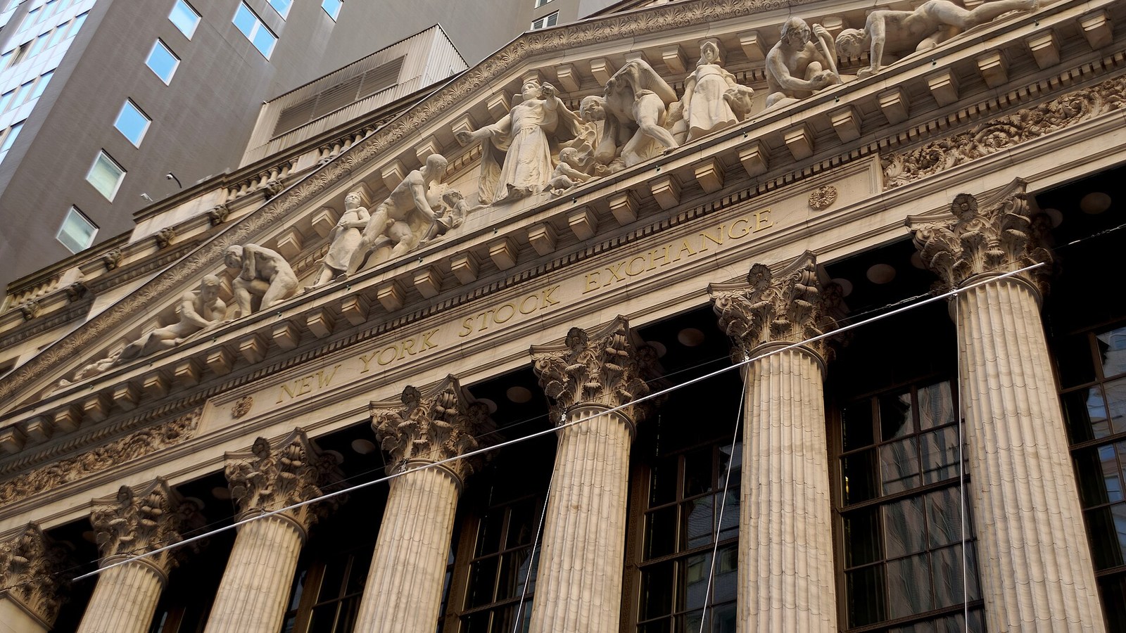 Low-angle view of the New York Stock Exchange facade, showing its name, Corinthian columns and stone sculptures.