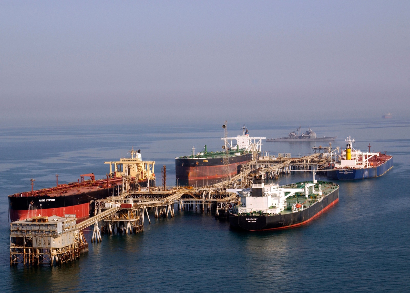 Oil tankers moored at the Al Basra Oil Terminal in the northern Persian Gulf, with a U.S. Navy cruiser on patrol behind them