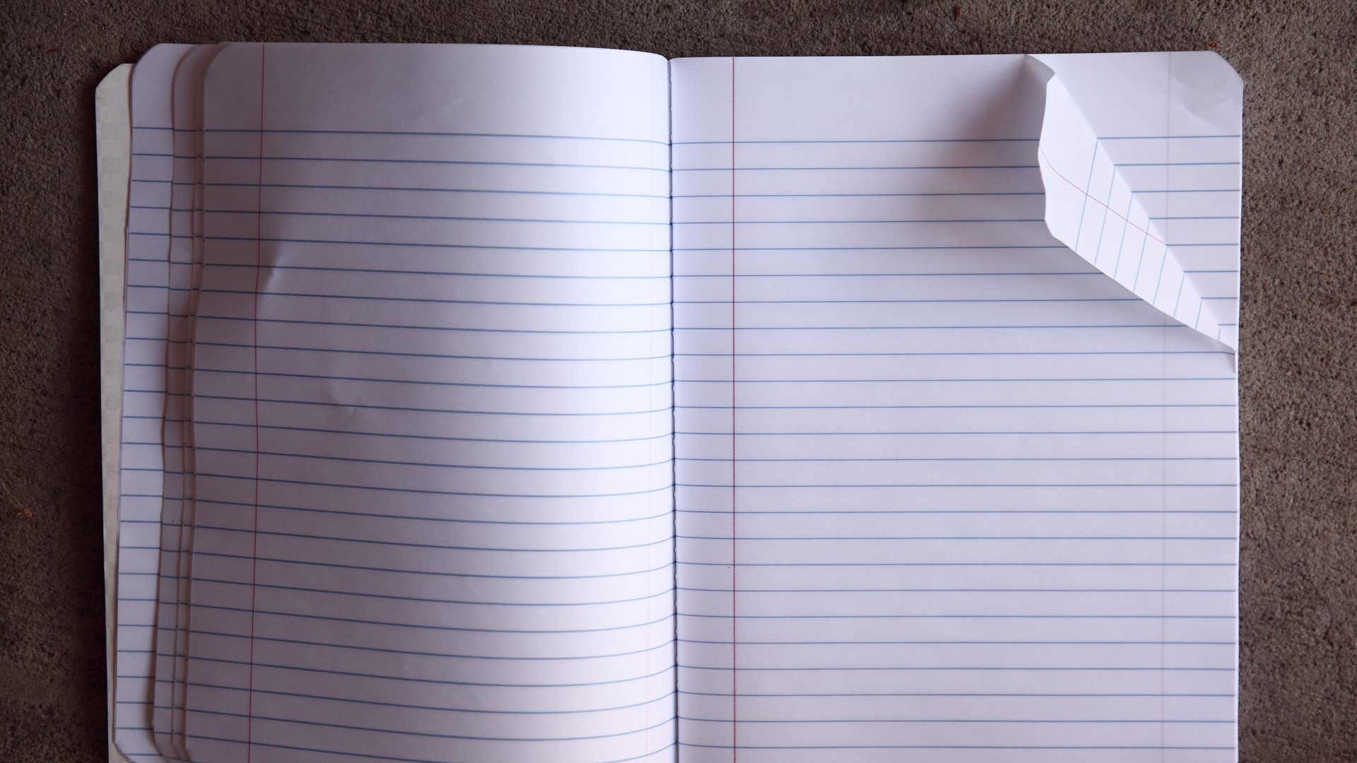 An open, blank, ruled notebook on a brown textured surface, with the upper-right page corner folded back.