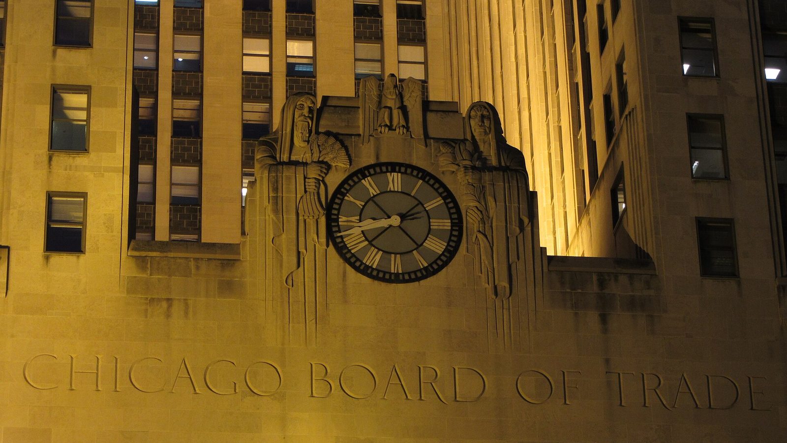 Une horloge éclairée et des sculptures en pierre sur la façade du Chicago Board of Trade, de nuit.