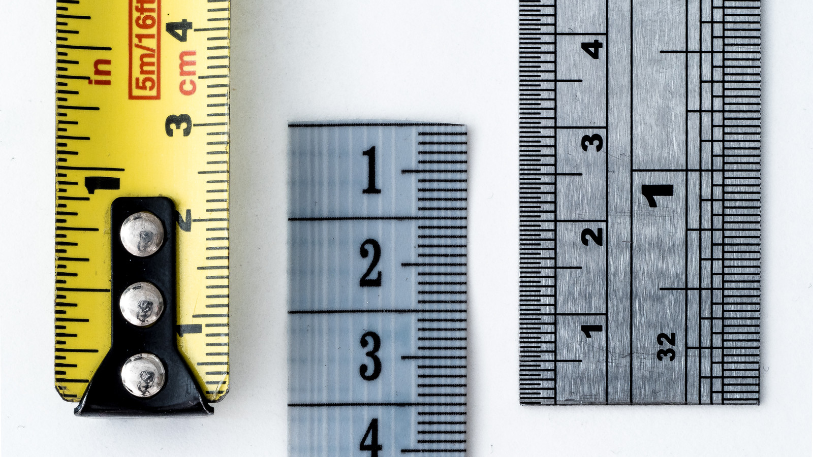 Close-up of a yellow tape measure marked in inches and centimetres, beside a pale measuring tape and a metal ruler on white.
