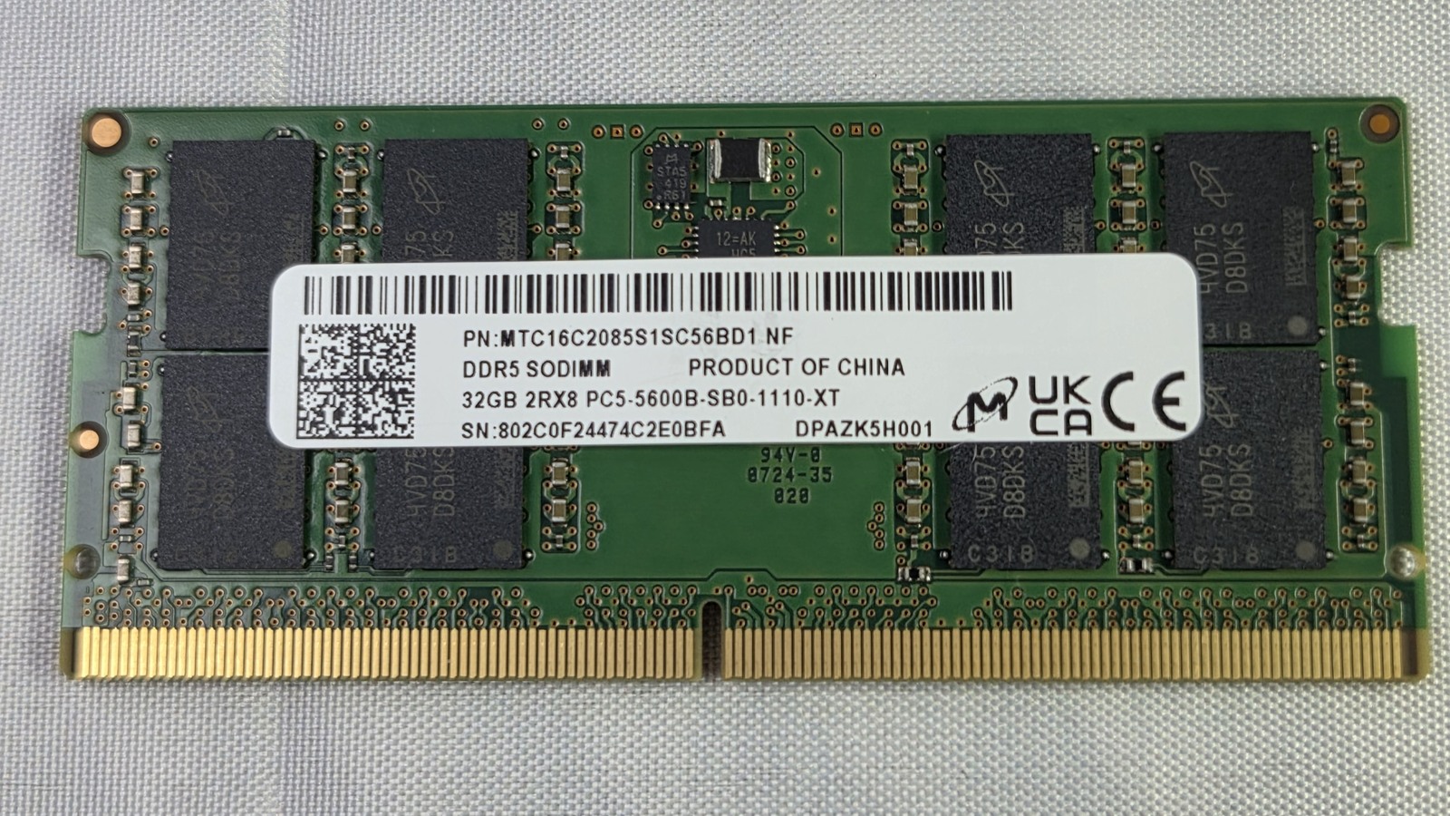 A green Micron memory module with black chips and a white product label on woven fabric.