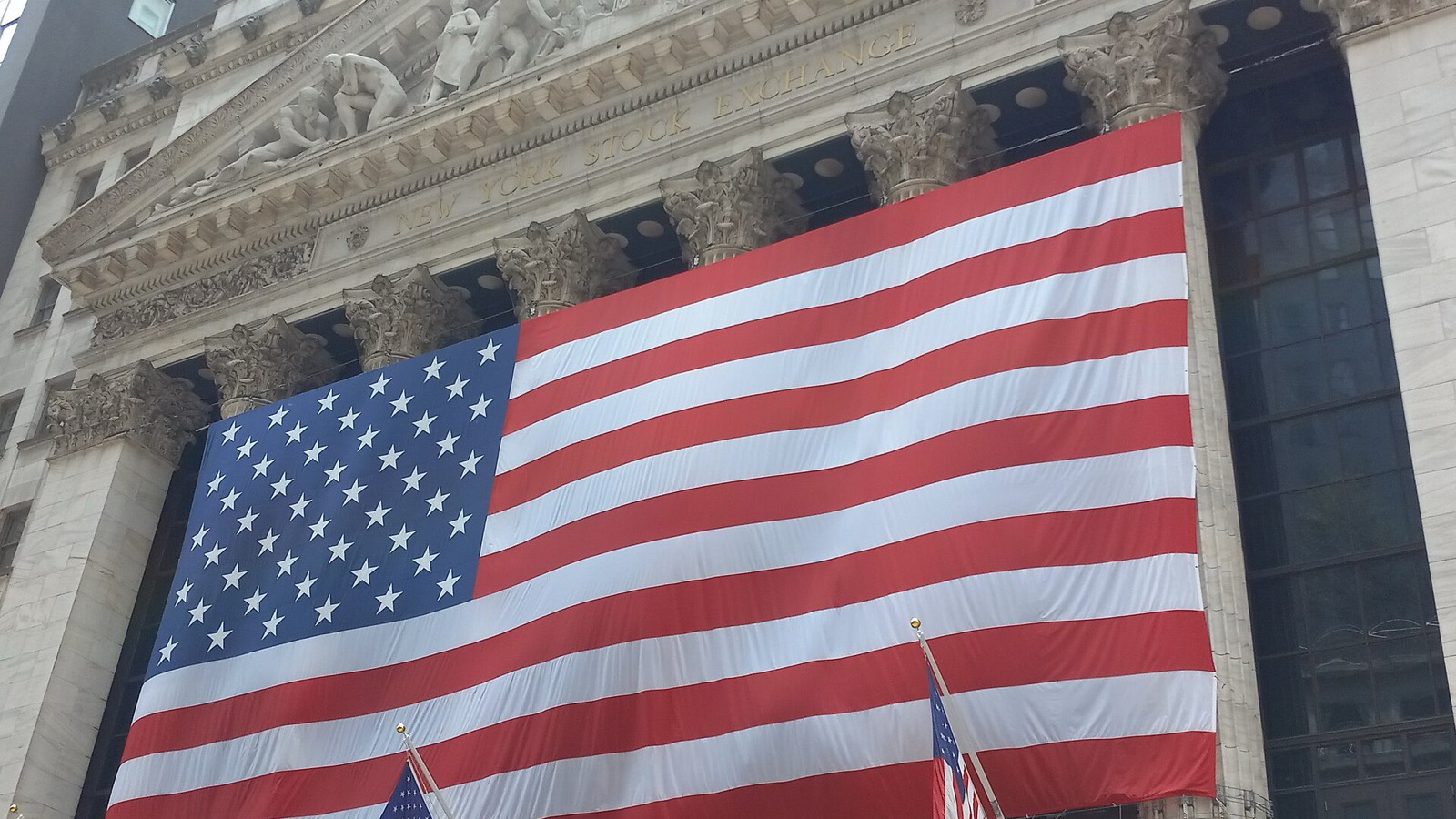 A large American flag across the stone facade and columns of the New York Stock Exchange