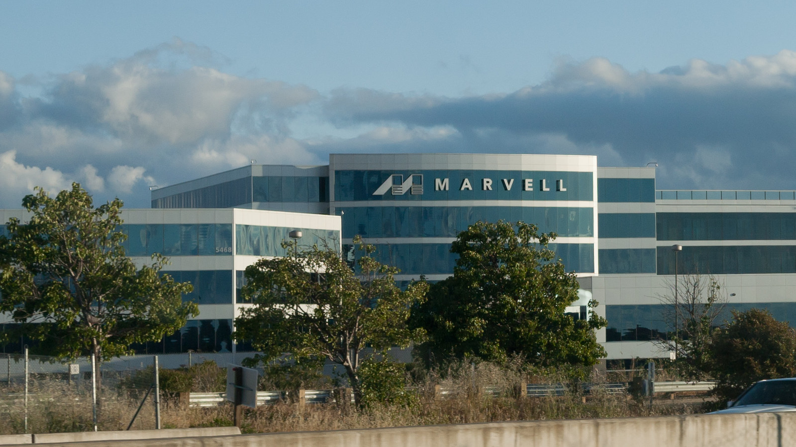 Photo d’archives de mai 2011 du siège de Marvell à Santa Clara, en Californie : façade blanche et vitrée bleu-vert, enseigne Marvell, arbres et clôture en bord de route.
