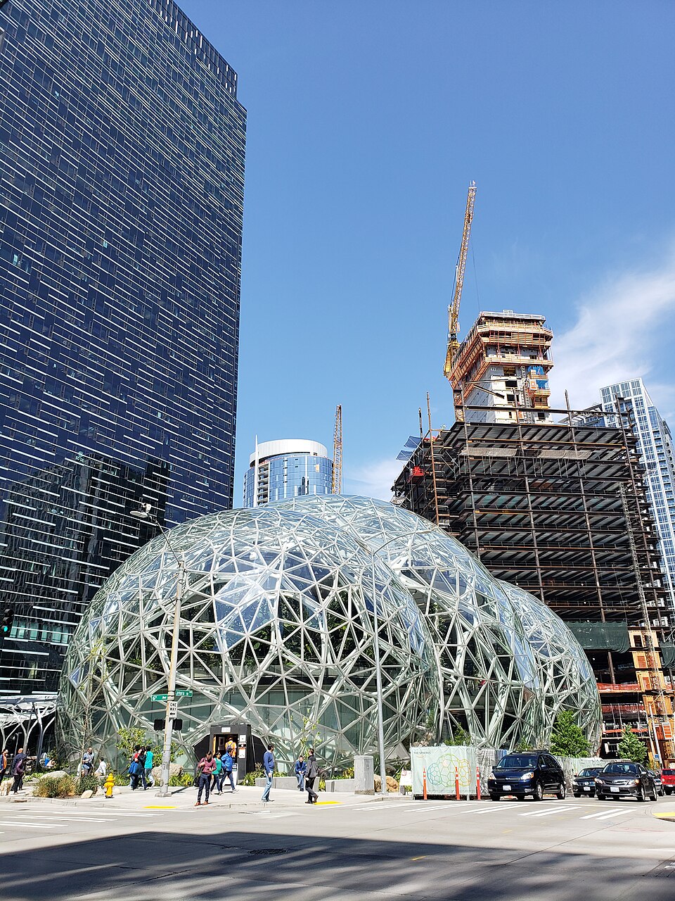 The glass domes of the Amazon Spheres in Seattle on a sunny day, with a tower under construction and a crane rising behind them
