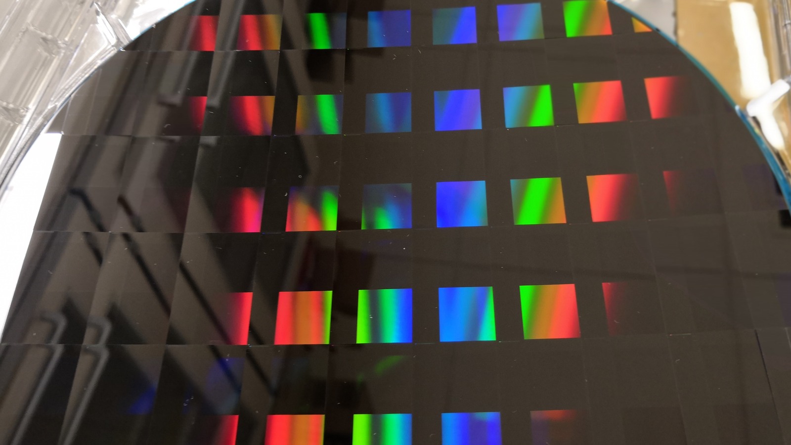 Archival close-up photograph of a dark patterned silicon wafer with rectangular reflections of red, green and blue light.