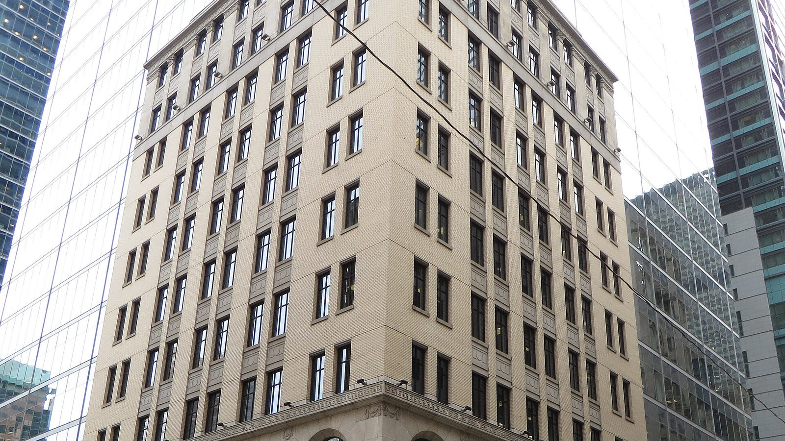 A pale brick office building surrounded by glass towers in Toronto’s Financial District.