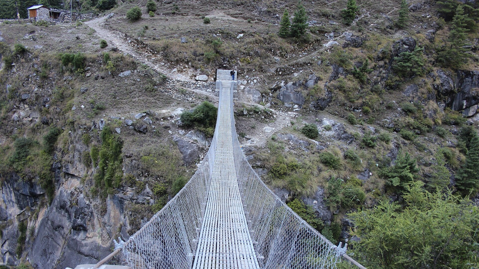 A narrow suspension footbridge crosses a rocky gorge in Nepal.