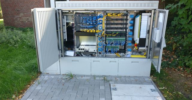 Open fibre-optic distribution cabinet with blue and yellow network cables and patch panels.
