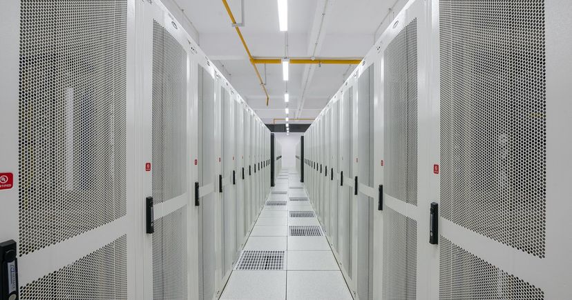 A long, brightly lit aisle between rows of white server racks in a data center