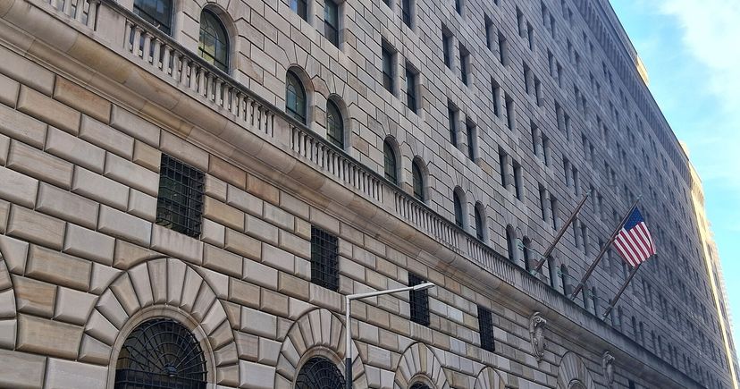 The stone facade of the Federal Reserve Bank of New York on Liberty Street, with an American flag