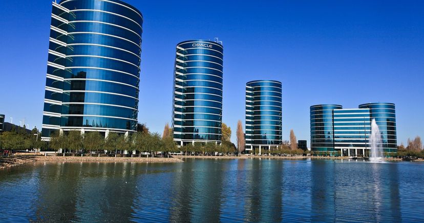Oracle's glass headquarters towers in Redwood Shores, California, reflected in a lagoon under a clear blue sky