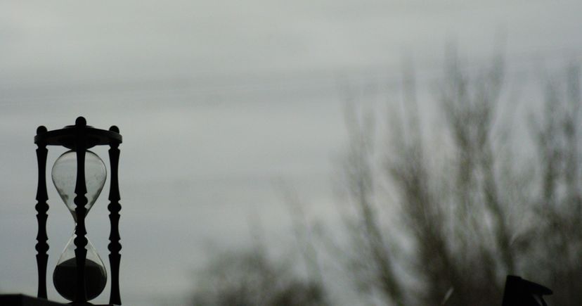 Sablier à monture sombre devant un ciel et des arbres dénudés flous