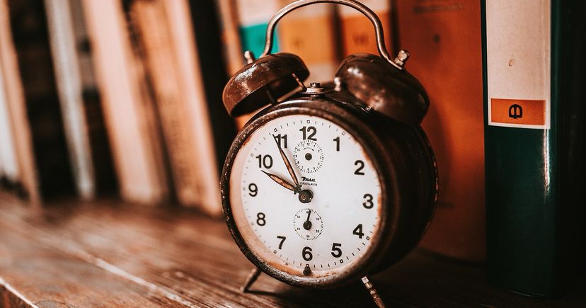 An old twin-bell alarm clock standing on a wooden bookshelf in front of books.