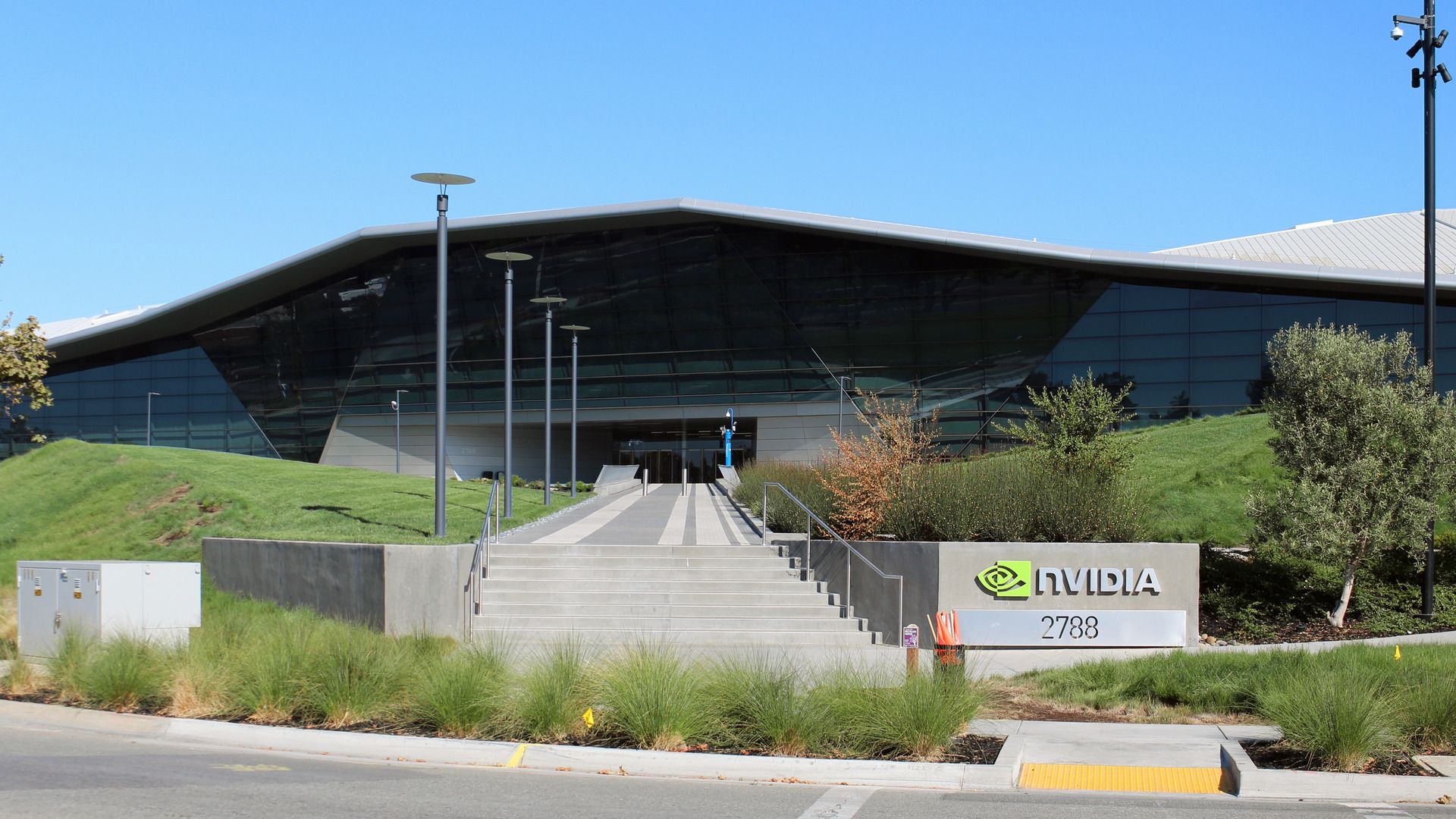 Archival August 2018 photograph of Nvidia's headquarters in Santa Clara, California, with a glass facade, landscaped slopes, stairs and a physical Nvidia sign.