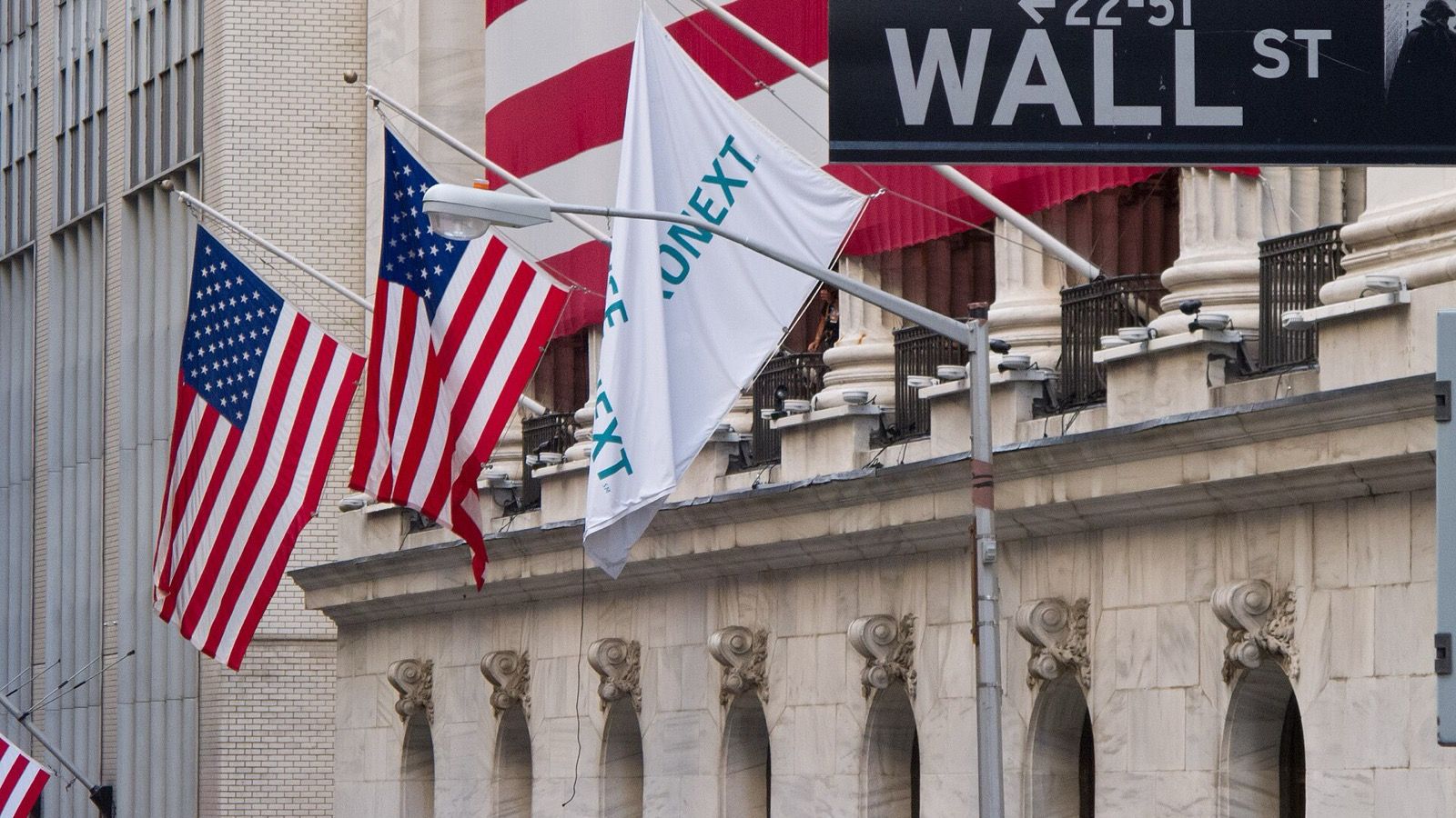 US flags, NYSE facade columns and a Wall Street sign in New York