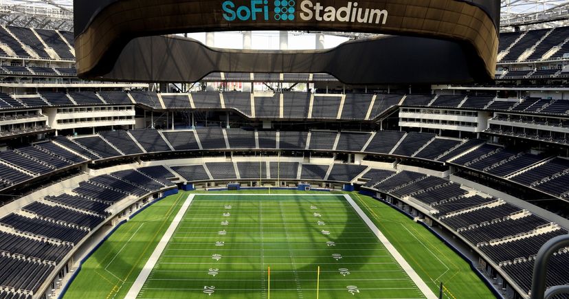 Archival March 2021 interior photograph of SoFi Stadium: an empty football field, blue seats and the SoFi Stadium name on the overhead display.