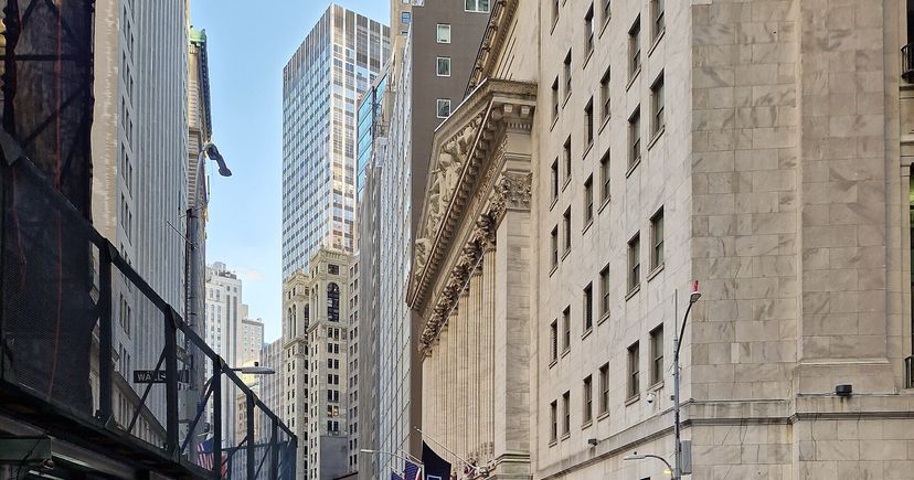 The stone exterior of the New York Stock Exchange along Wall Street, beside neighboring office buildings