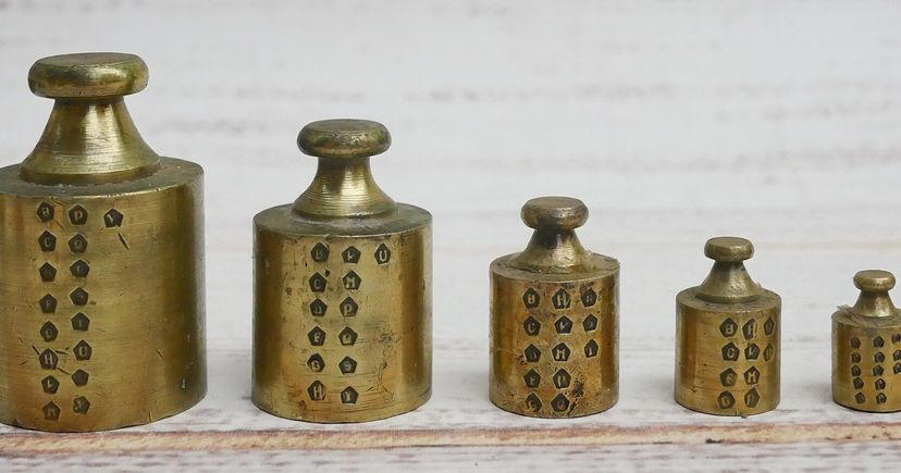 Cinq poids en laiton de tailles différentes alignés sur une surface en bois